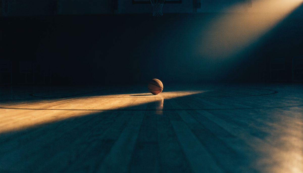 An empty basketball court at night with a single ball at the free-throw line