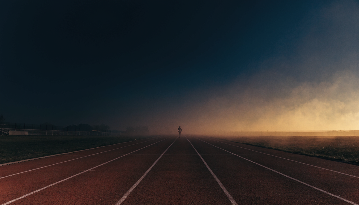 An outdoor running track at dusk with lane lines receding into the distance