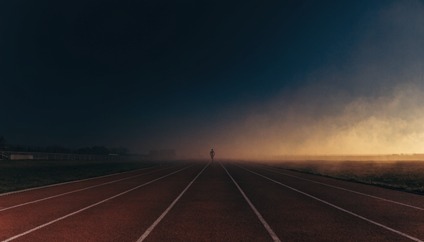 An outdoor running track at dusk with lane lines receding into the distance